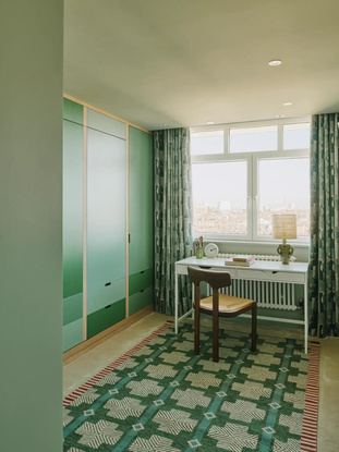 Рабочая зона и гостевая комната с зелёными шкафами и большим окном: функциональное решение для работы дома с видом на лондонские постройки.