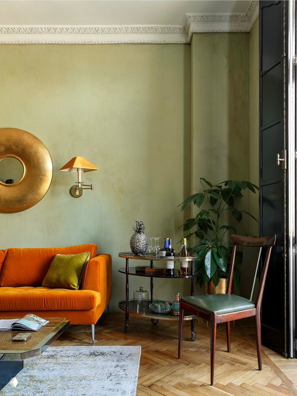 Уютная гостиная с барной тележкой, оранжевым диваном и зелёной стеной — сочетание винтажа и ярких акцентов в интерьере.