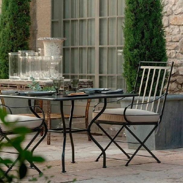 Металлическая складная мебель — стальные стулья и стол на патио у каменной стены, лёгкий ретро-шарм и нейтральные подушки.