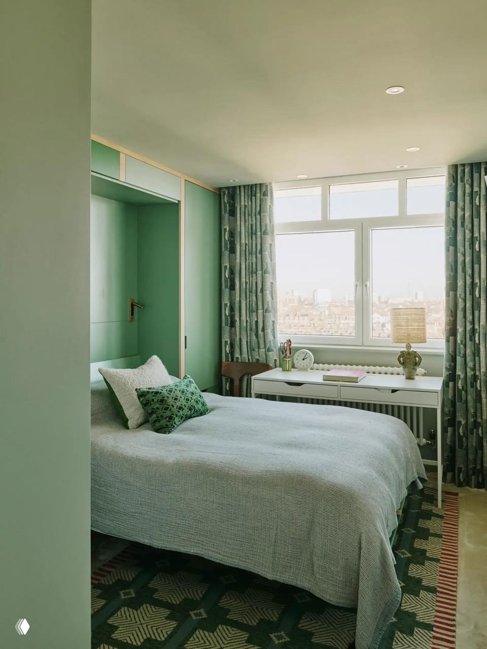 Спальня с зелёными встроенными шкафами, ковром с геометрическим рисунком и продуманной планировкой, сочетающей рабочее место и зону отдыха.