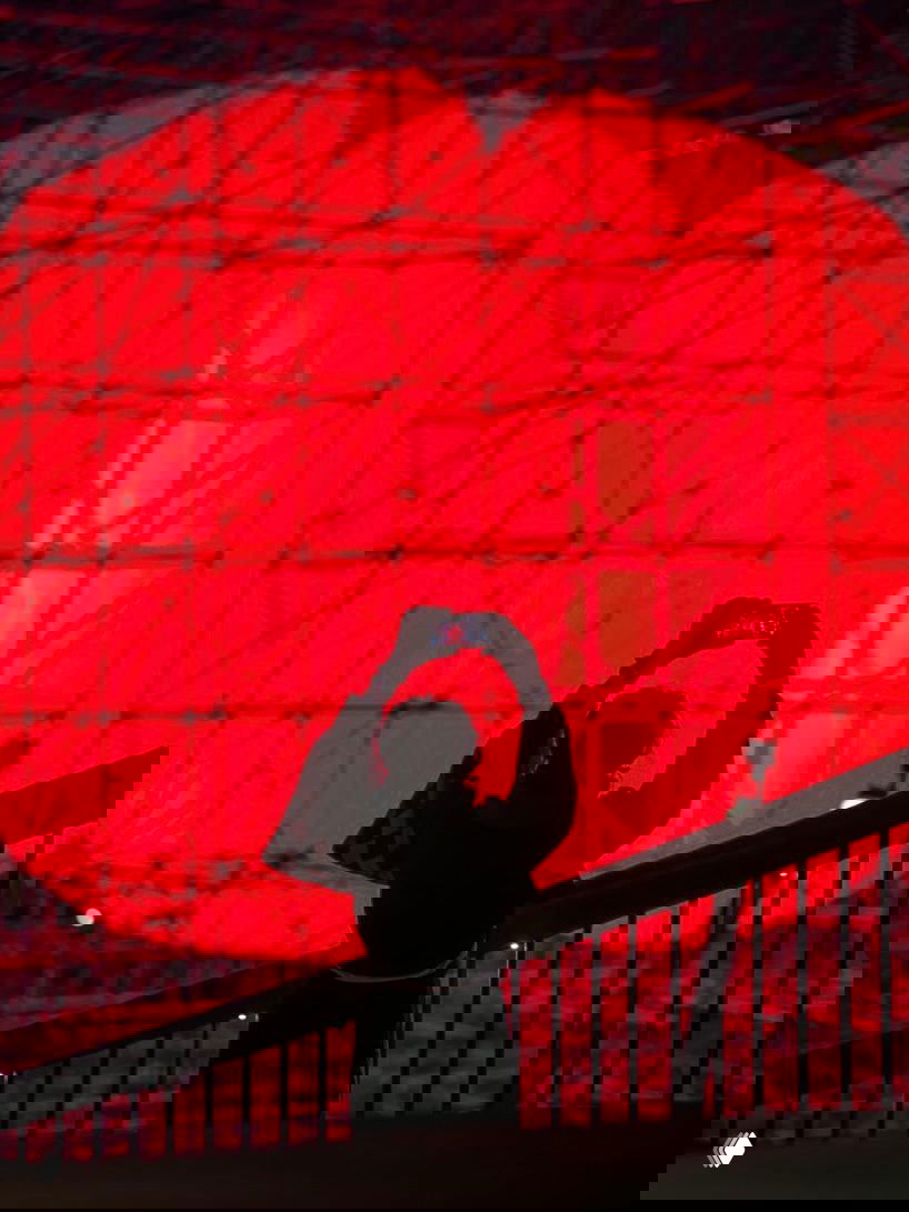 Силуэт человека с телефоном на переднем плане на фоне огромной ярко красной сферы-инсталляции: контраст света и тени.