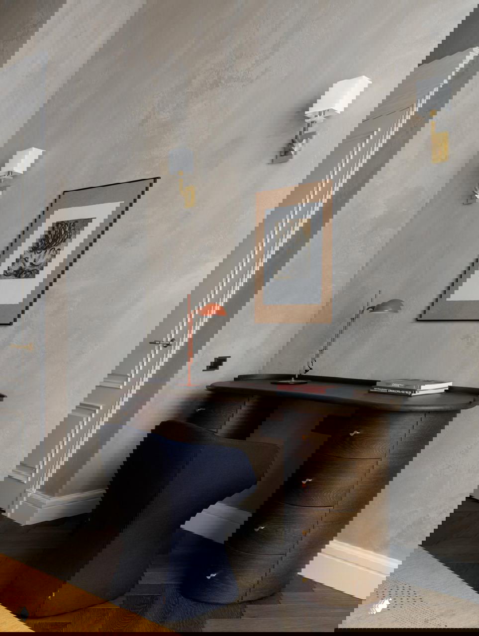 Рабочая зона в квартире: тёмный округлый письменный стол из дерева, тёмно-синее кресло и нейтральная отделка стен с арт-обрамлением в стиле французского шика