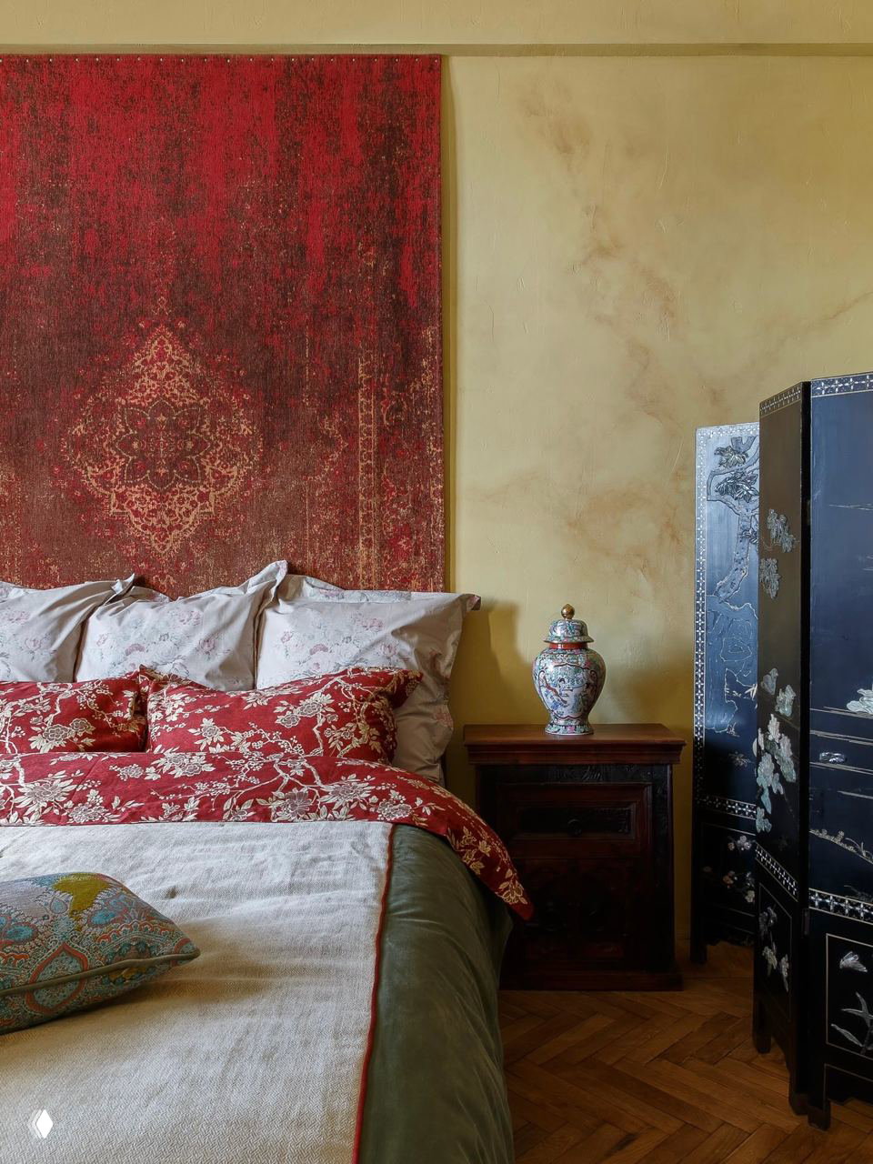 Спальня с текстильным панелйом в красных тонах за изголовьем, восточными вазами и декоративным ширмой — пример эклектичного декора.