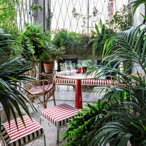 Компактный обеденный гарнитур с красно‑белыми полосатыми сиденьями и зелёными растениями вокруг, уютная зимняя веранда.