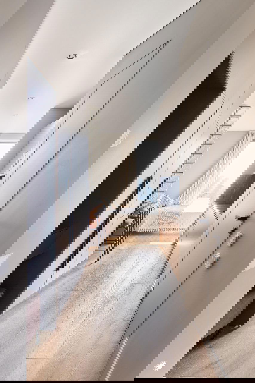 Узкий коридор с деревянным полом, встроенные шкафы и перегородка из стеклоблоков, в конце — окно с видом на Москва‑сити.