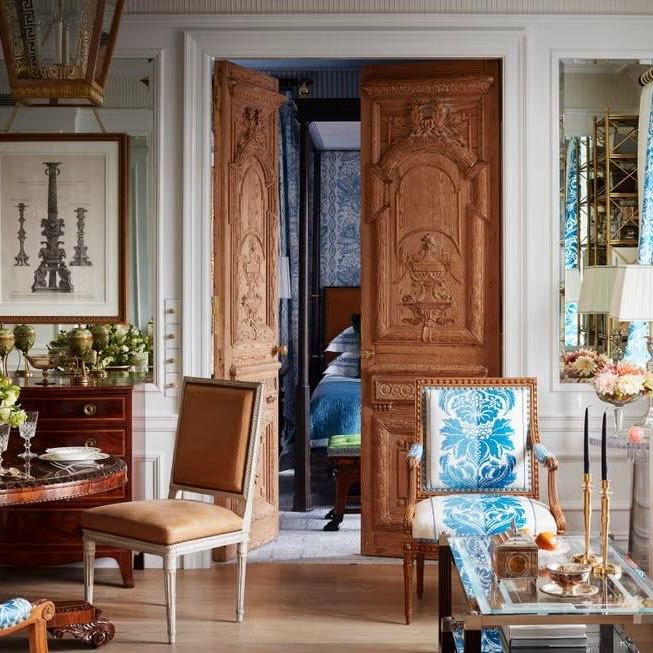 Гостиная с резными деревянными дверями и смелым сочетанием кресел и столиков — пример смешения антиквариата и ретро-мотивов в интерьере.