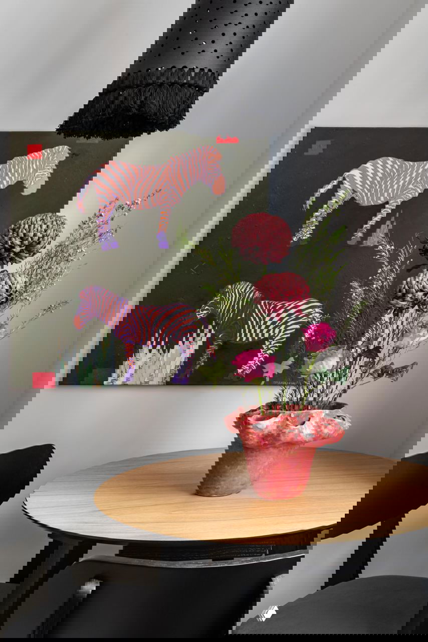 Крупный план картины с зебрами над столом, текстурная ваза с букетом и подвесной плафон с бахромой — винтажные детали в компактном уголке.