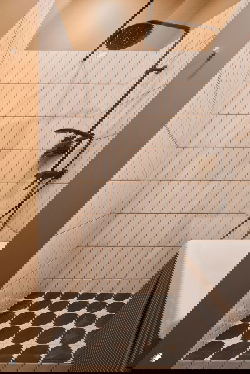 Компактная душевая кабина с белой прямоугольной плиткой, черной душевой колонкой и контрастной геометрической плиткой на полу.