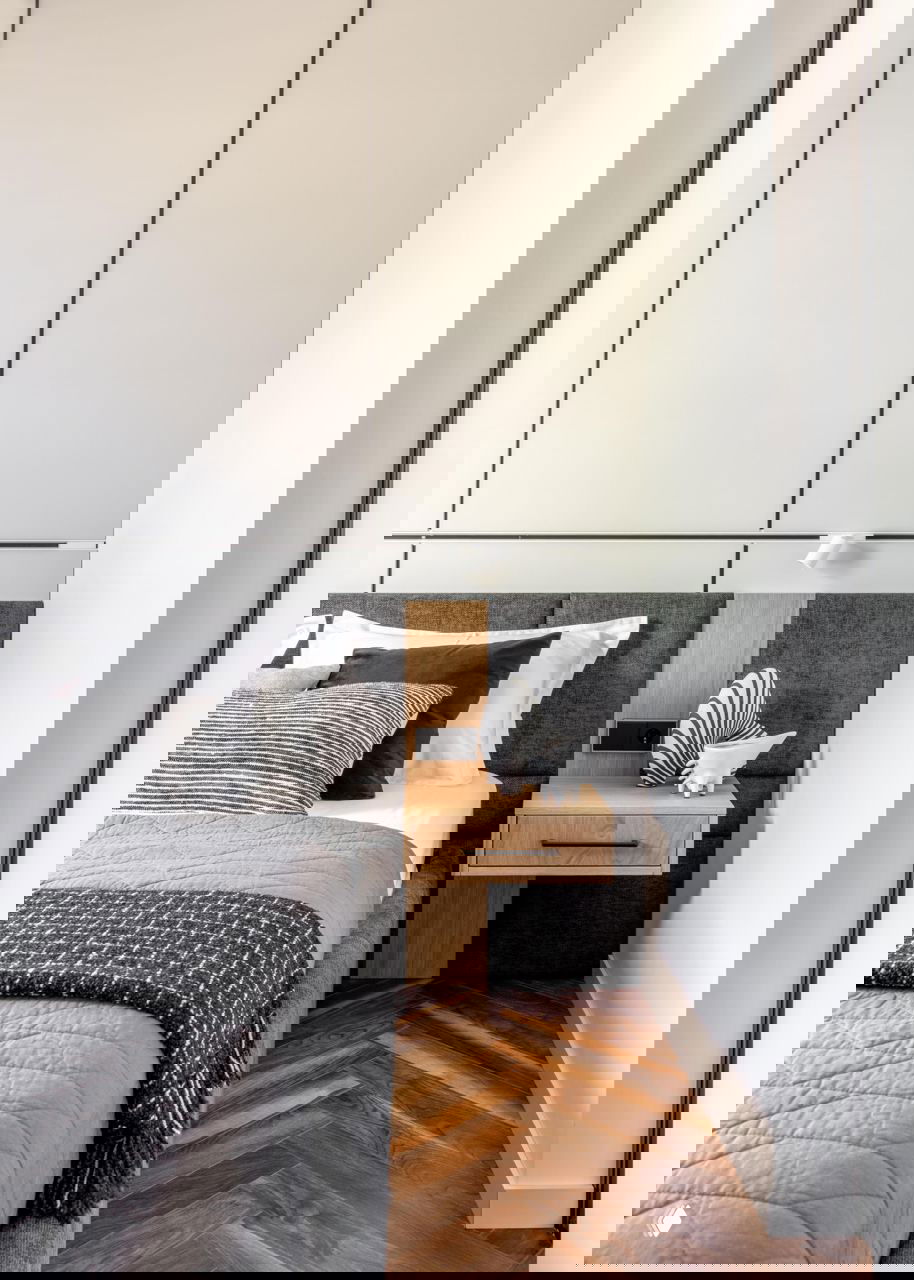 Фрагмент интерьера спальни: прикроватная тумба из светлого дерева, изголовье из тёмной обивки и минималистичный декор в монохромной гамме.