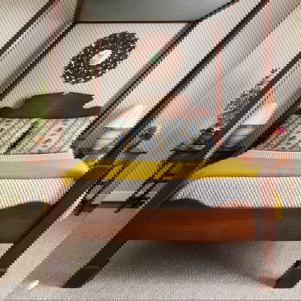 Четырехколонная деревянная кровать в традиционном стиле с узорными подушками и жёлтым пледом — пример использования антиквариата в спальне.