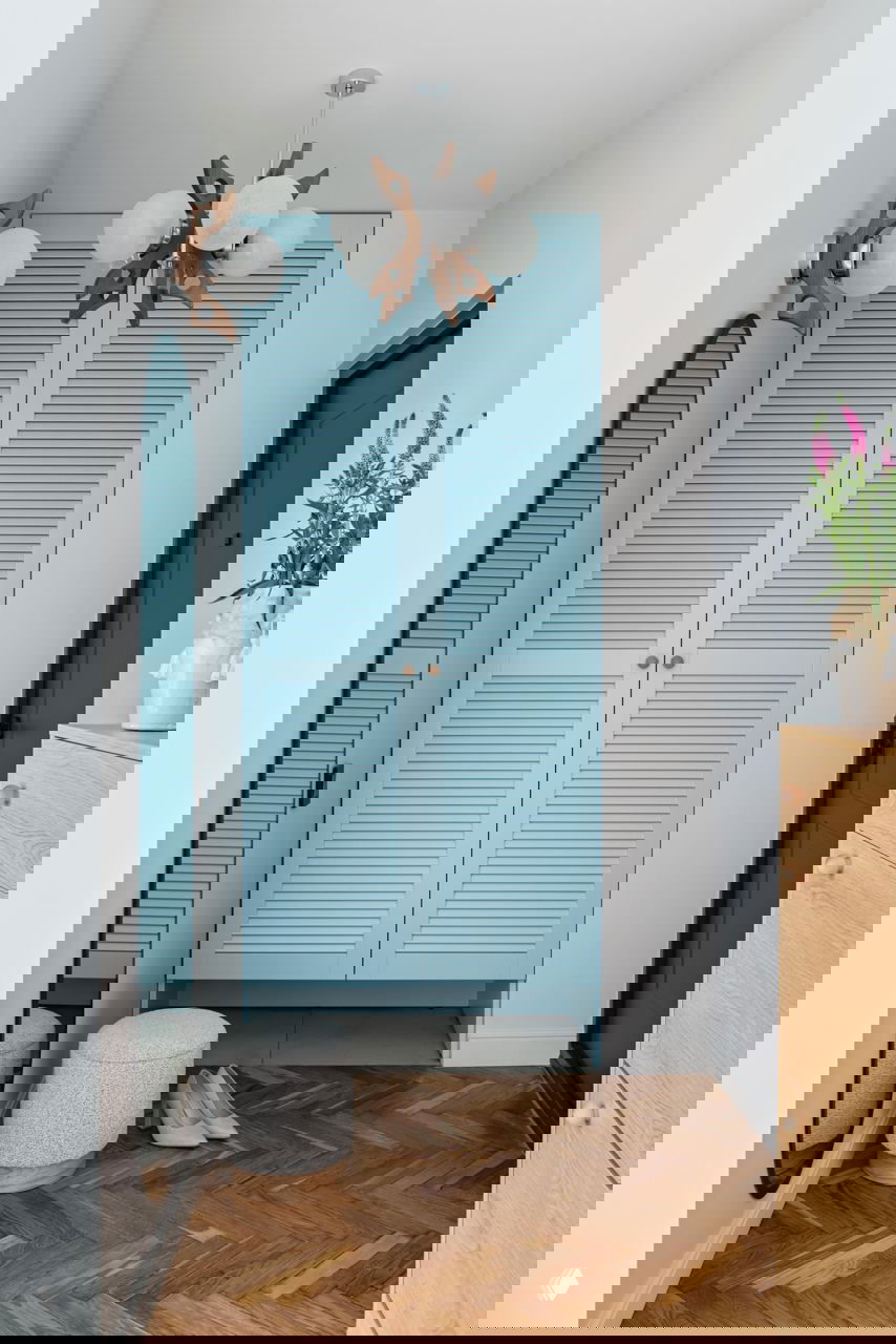 Прихожая с голубыми жалюзийными дверцами шкафа, зеркалом в полный рост, паркетом «ёлочкой» и винтажной люстрой — сочетание старого паркета и новых акцентов.