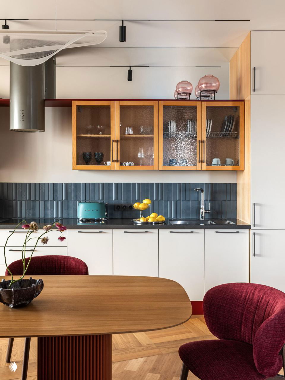 Кухня-столовая: голубой плиточный фартук, деревянные витрины с рифлёным стеклом, белые нижние фасады и тёплый деревянный обеденный стол.