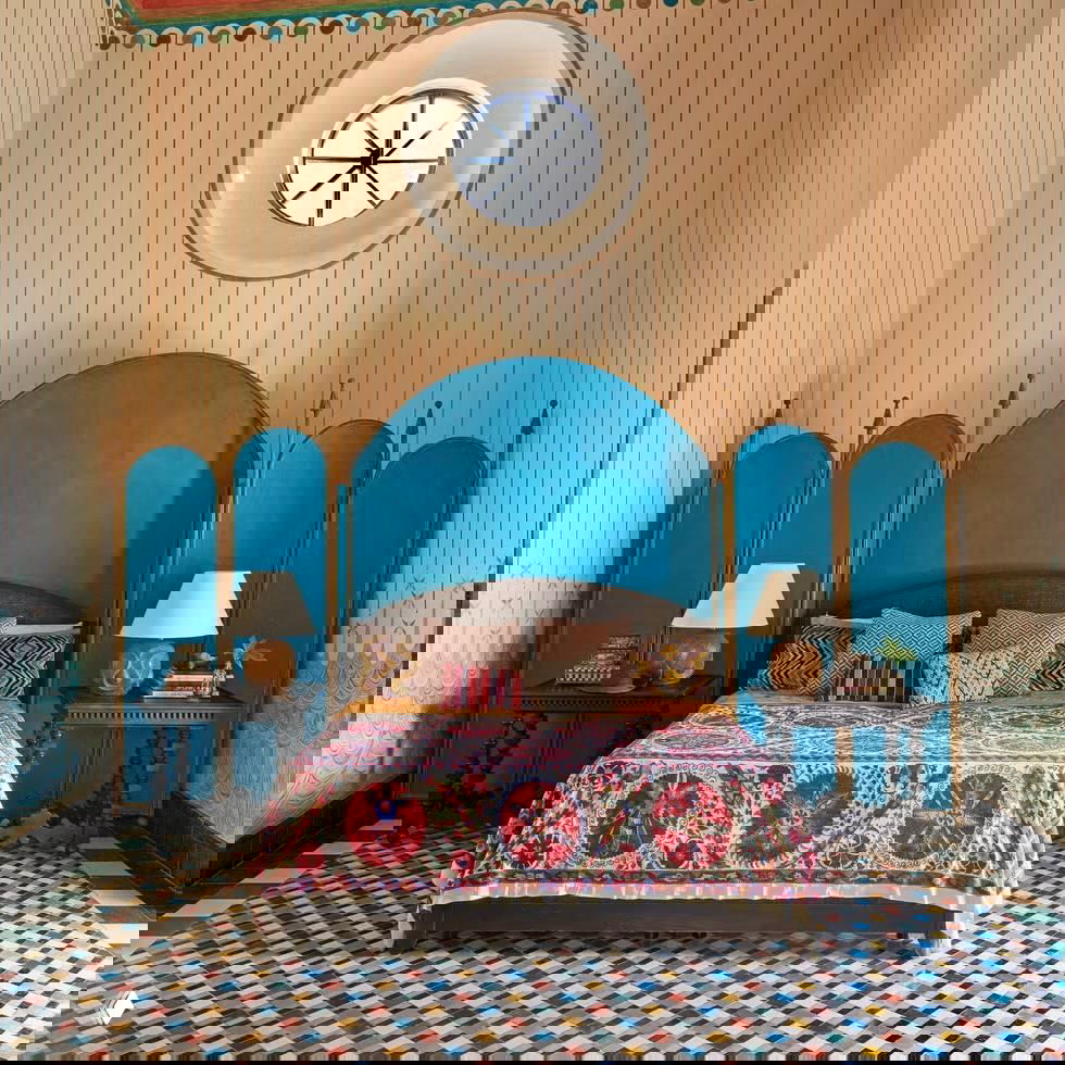 Яркая спальня с голубым изголовьем, этническим покрывалом и мозаичным полом — сочетание восточного влияния и винтажного декора.