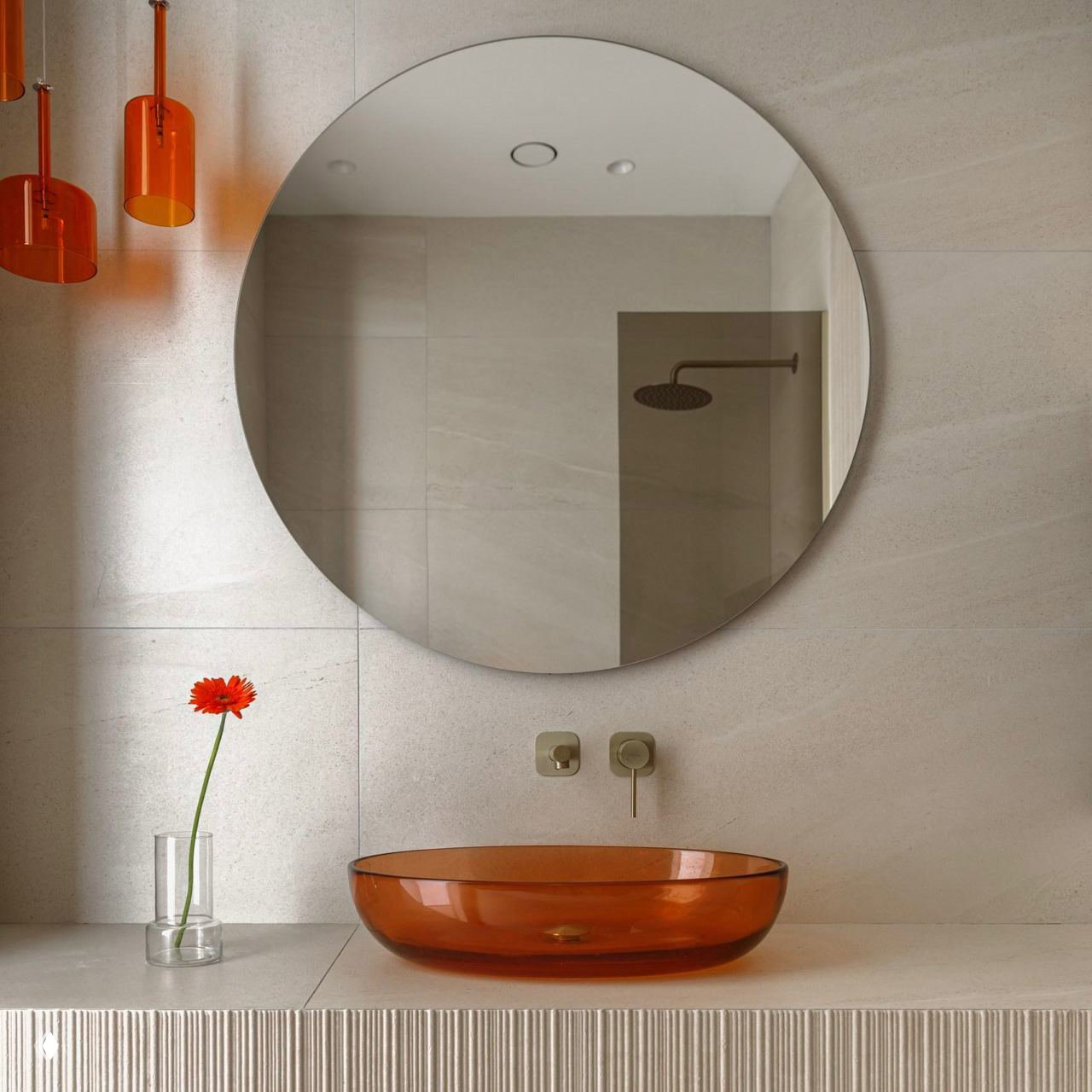 Светлая минималистичная ванная с большим круглым зеркалом и прозрачной оранжевой накладной раковиной на светлой столешнице