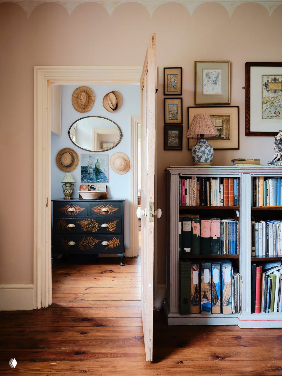 Коридор и кабинет: дверь приоткрыта, комод с росписью, настенные шляпы и стеллаж с книгами — детали, создающие ощущение давней обжитости.