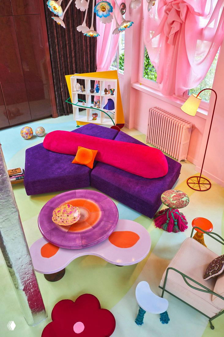 Гостиная с модульным фиолетовым диваном, розовыми портьерами, цветными столиками и пастельным полом — причудливые формы мебели и текстиля.