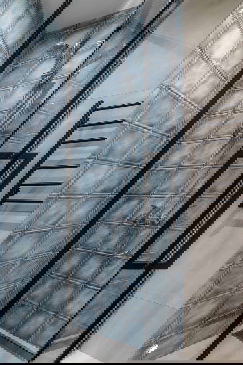 Душевая кабина с квадратной синей плиткой в стеклянной перегородке и чёрной металлической фурнитурой — текстурный контраст в небольшой ванной.