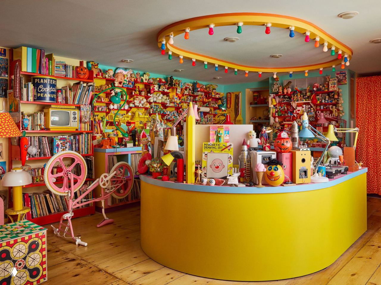 Комната, похожая на магазин игрушек: круглая барная стойка, стенды с винилом и множеством цветных объектов — театрализованное пространство коллекций.