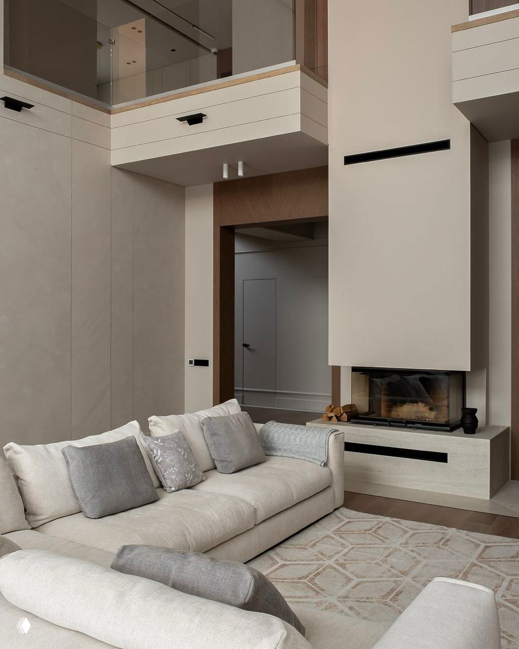 Гостиная с двойной высотой потолка: светло-бежевая мебель, просторный диван и минималистичный камин в нейтральной отделке интерьера.
