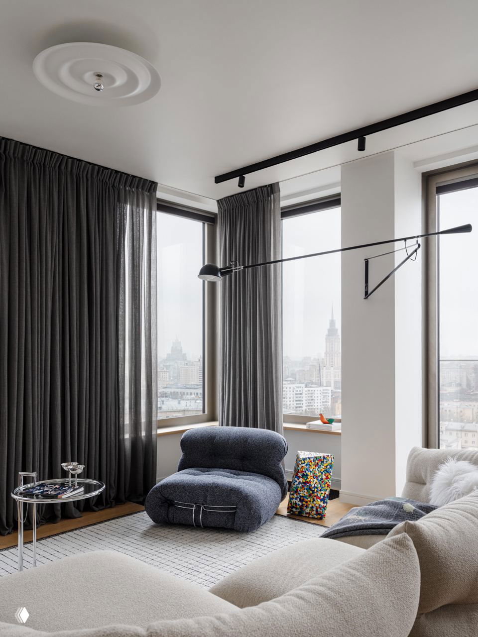 Уютный уголок у панорамных окон: мягкое кресло-пуф, большой ковёр и вид на город через высокие окна в московской квартире.