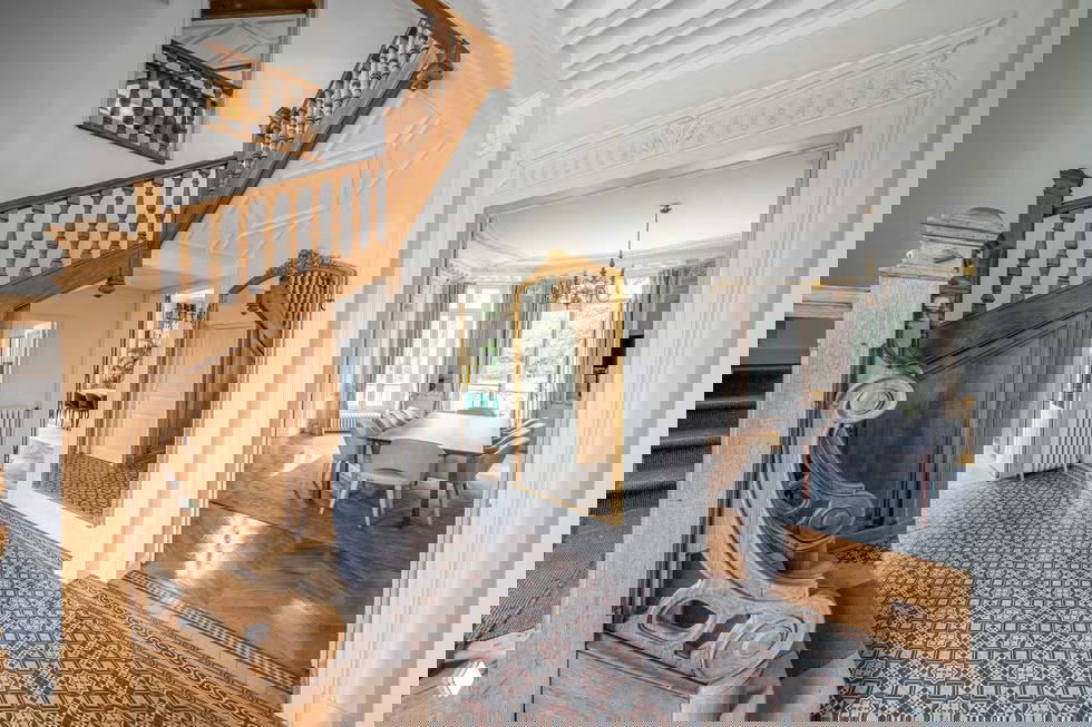 Интерьер вестибюля особняка с резной деревянной лестницей, кессонным потолком и декоративной напольной плиткой — сохранённые исторические детали интерьера.