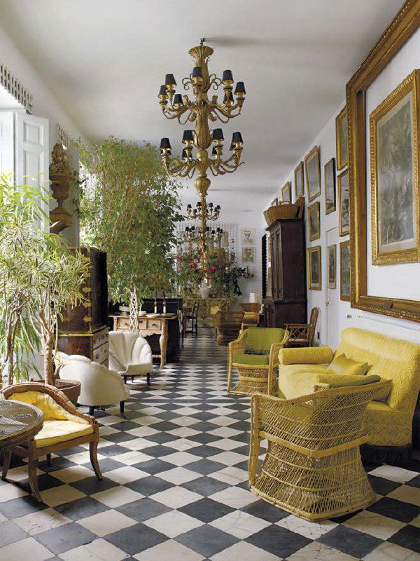 Длинный зал-галерея с черно‑белым шахматным полом, плетёной и антикварной мебелью — пример классического узорного покрытия, возвращающегося в тренды.