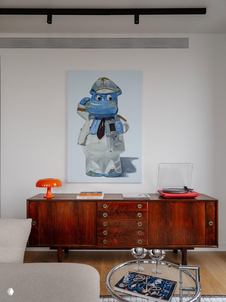 Комод из тёмного дерева с ретро-акцентами, настольная лампа с оранжевым абажуром и современная картина над интерьером.