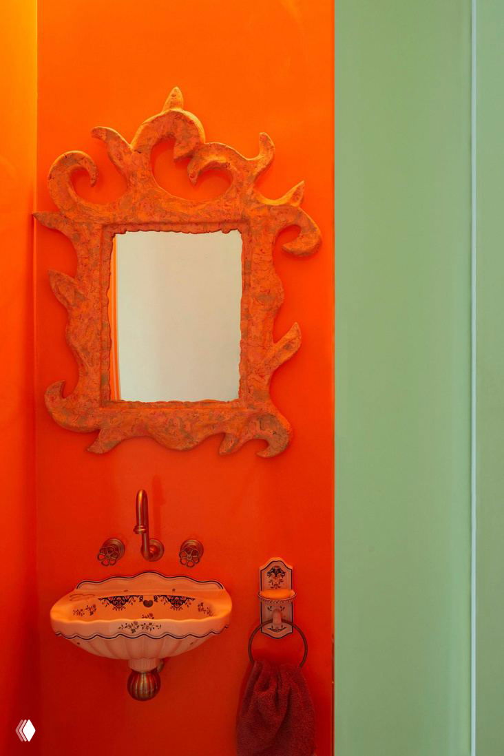 Розовая ванная с пастельными стенами и зеленой тумбой, декоративными зеркалами и мягким ковриком‑цветком — мягкая цветовая гамма и ретро-элементы.