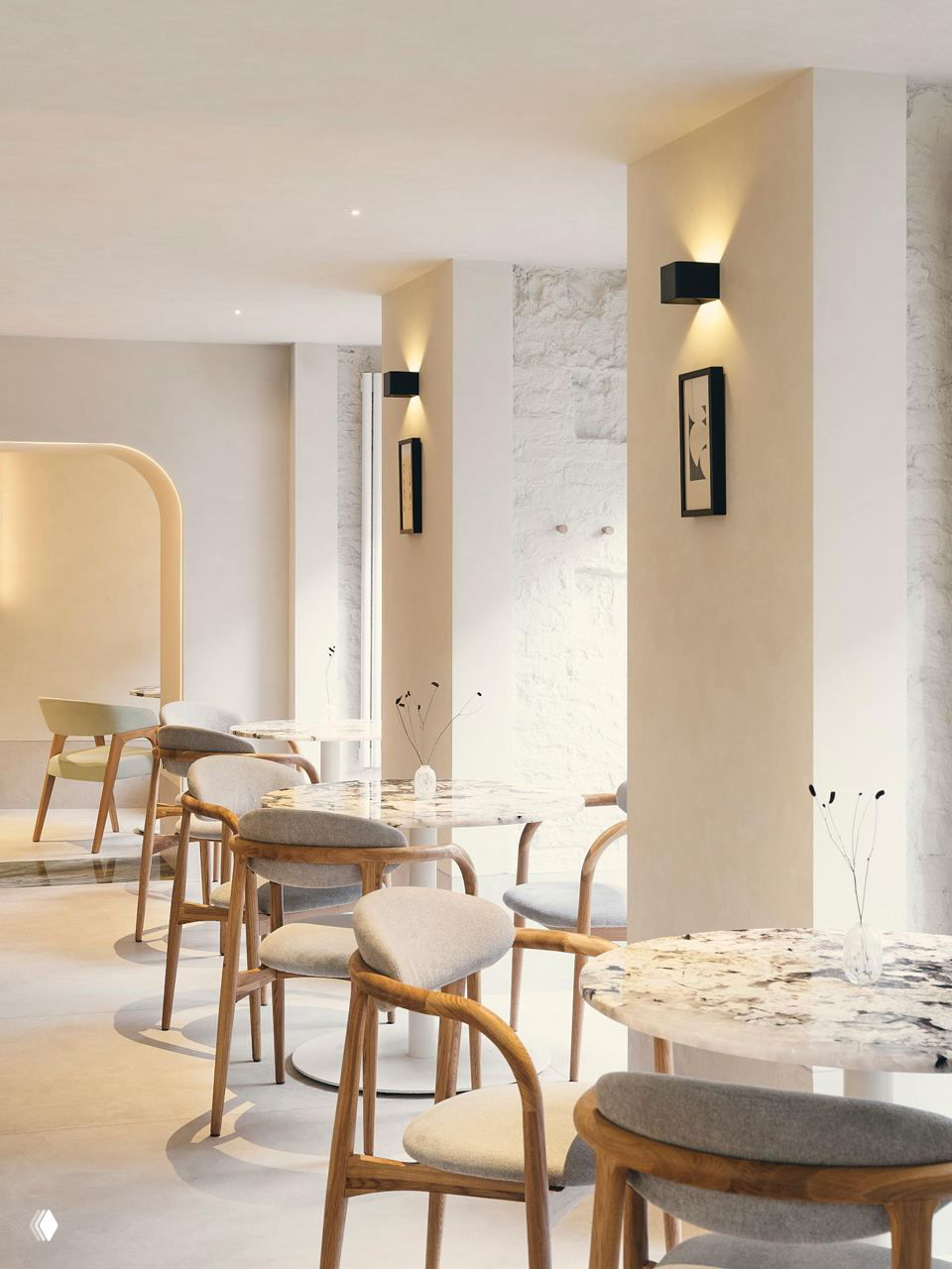 Ряд круглых столов с мраморными столешницами и деревянными стульями в светлом зале ресторана: микровелюр, мягкие сиденья и минималистичная декоративная штукатурка.