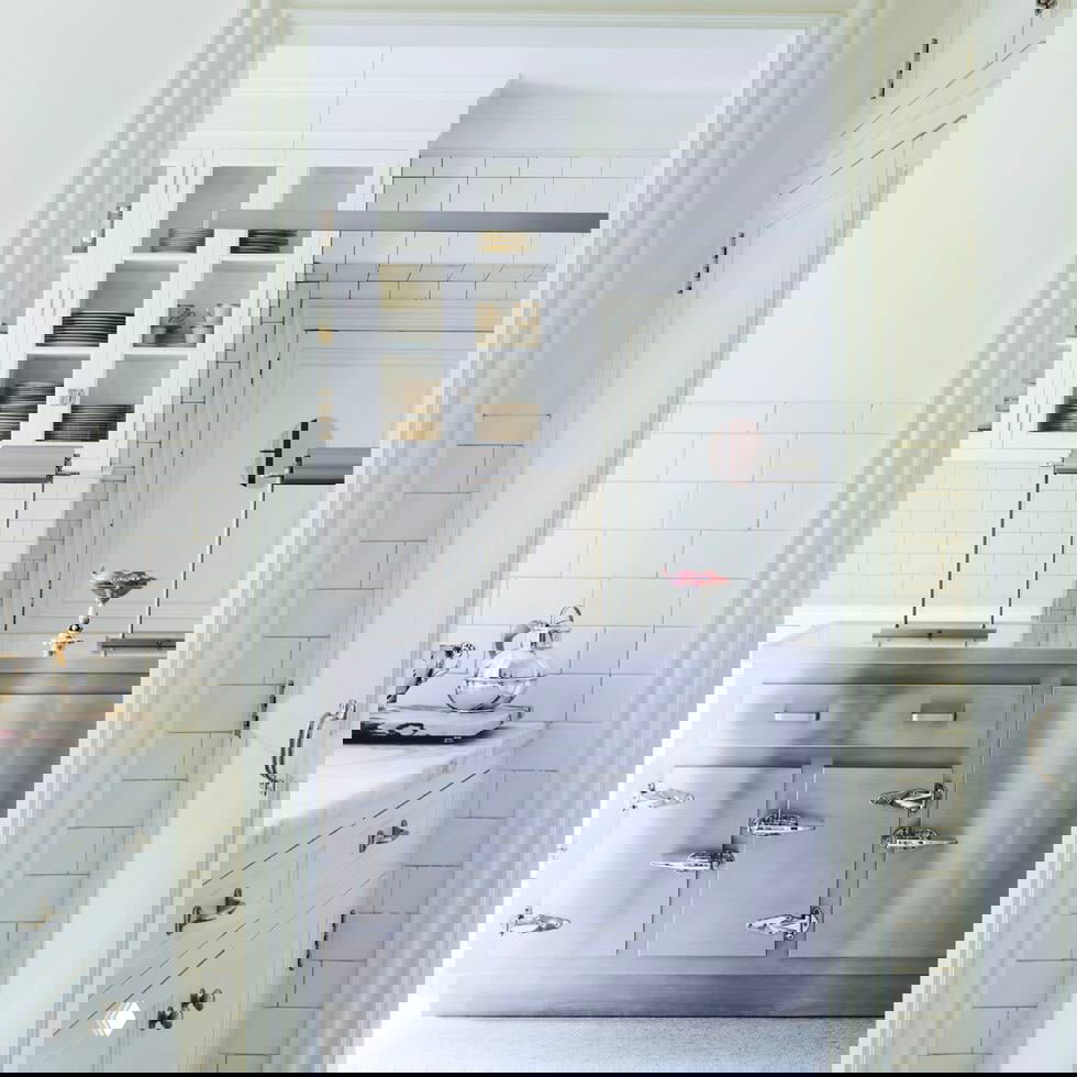 Кухня особняка в светлых тонах: остров с металлической отделкой, белая плитка в стиле метро и встроенные шкафы с посудой