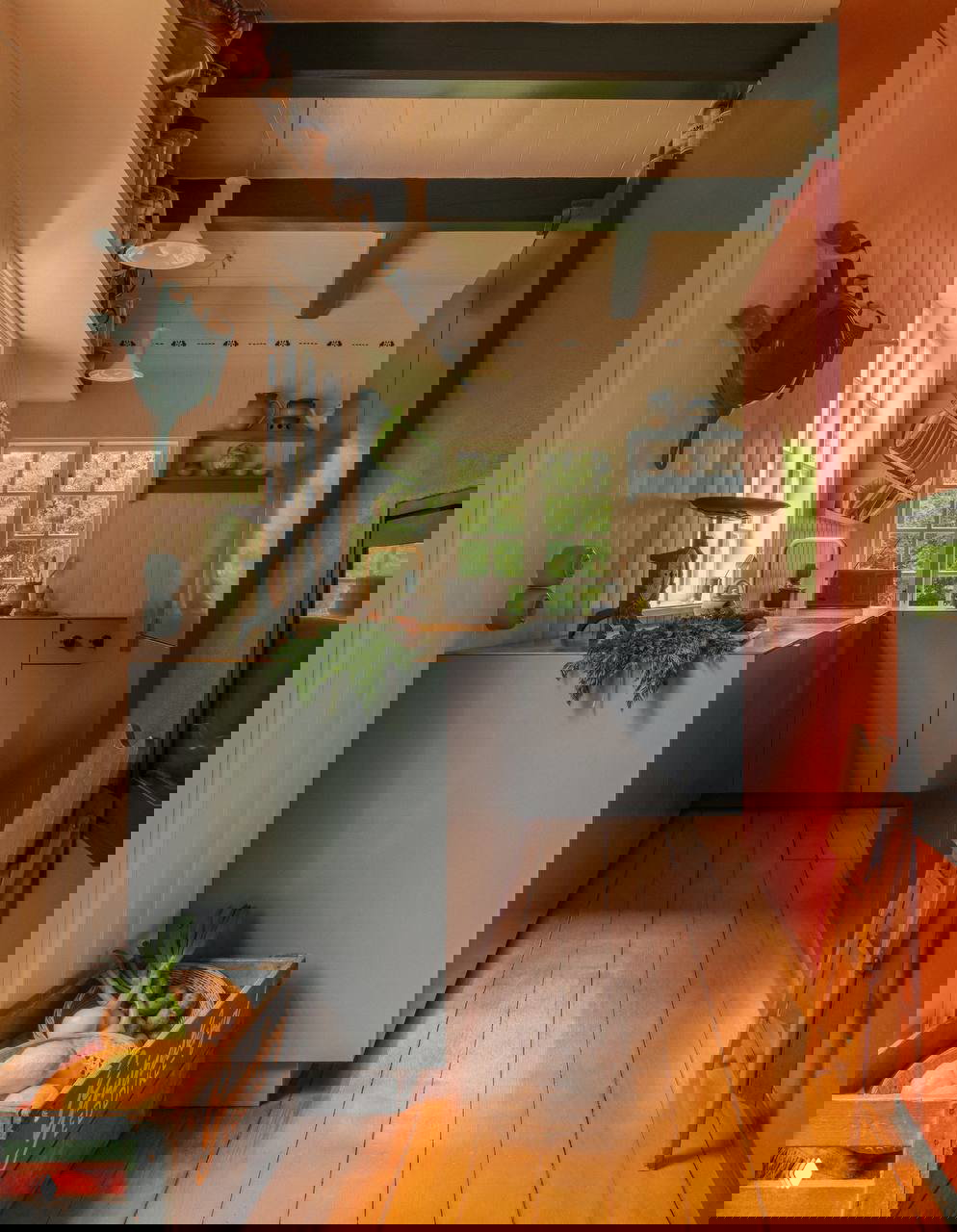 Уютная кухонная зона в светлых тонах и контрастных синих шкафах, деревянный пол и окно с видом на зелень — пример тёплого скандинавского интерьера внутри домика.