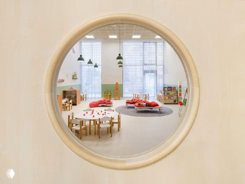 Открытое учебное пространство с большим окном и мягкими зонами для спокойных занятий; интерьер ориентирован на взаимодействие и естественный свет.