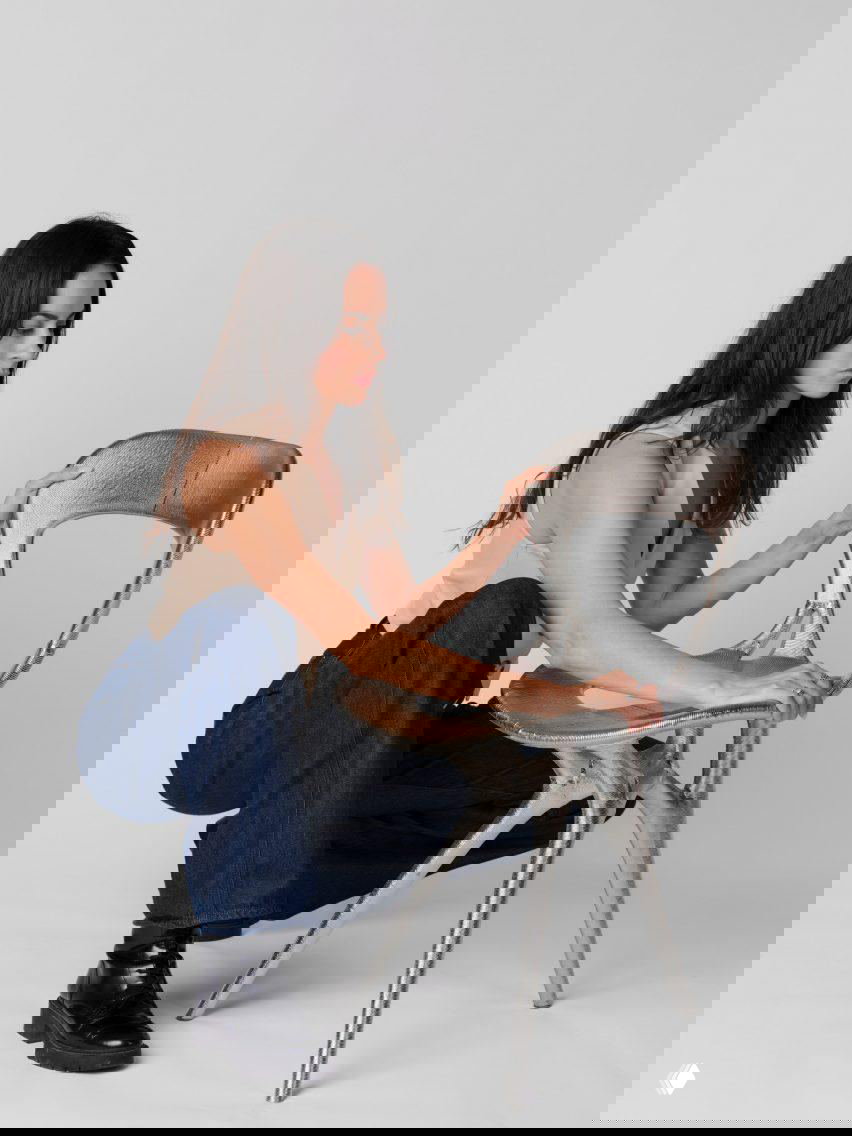 Женщина садится рядом с металлическим креслом из 3D-печати, примеряя посадку и оценивая форму сиденья и спинки в студийной съёмке.