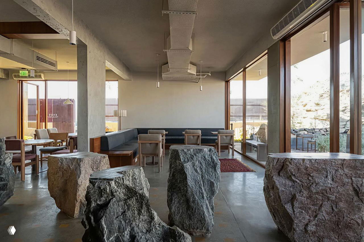 Зал кафе с большими окнами и грубыми каменными столами-валунами на полированном полу, сочетание мебели и скульптуры в интерьере Movs Studio.