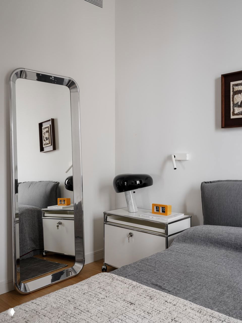 Спальня с высоким зеркалом в хромированной раме, прикроватной тумбой в индустриальном стиле и мягким текстилем на кровати.