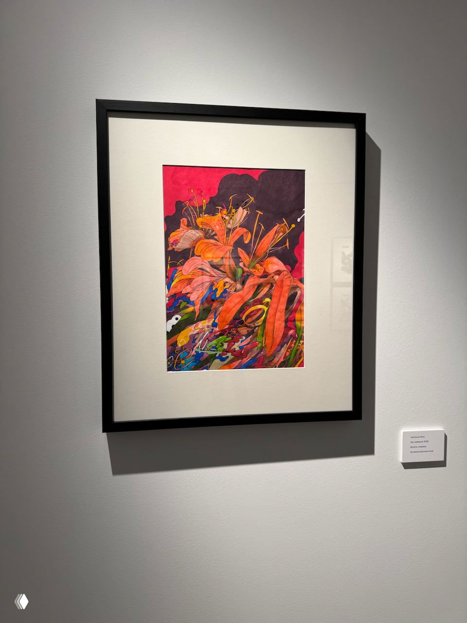 Оформленная в рамку цветная работа с яркими растительными мотивами висит на белой стене под точечным светом в экспозиции.