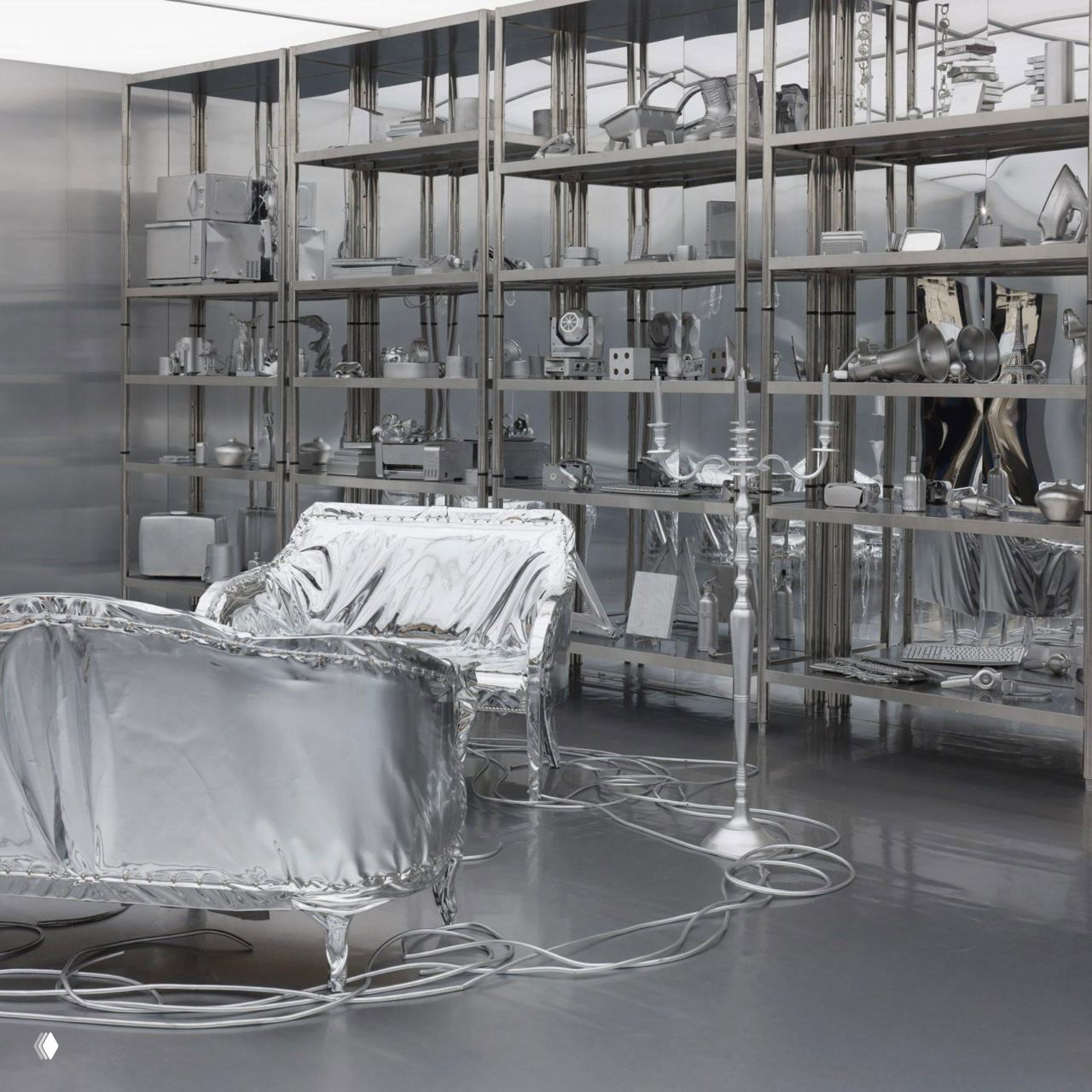 Крупный план диванов и стола, окутанных отражающей серебристой тканью; на заднем плане металлические стеллажи с историческими предметами и деталями экспозиции.