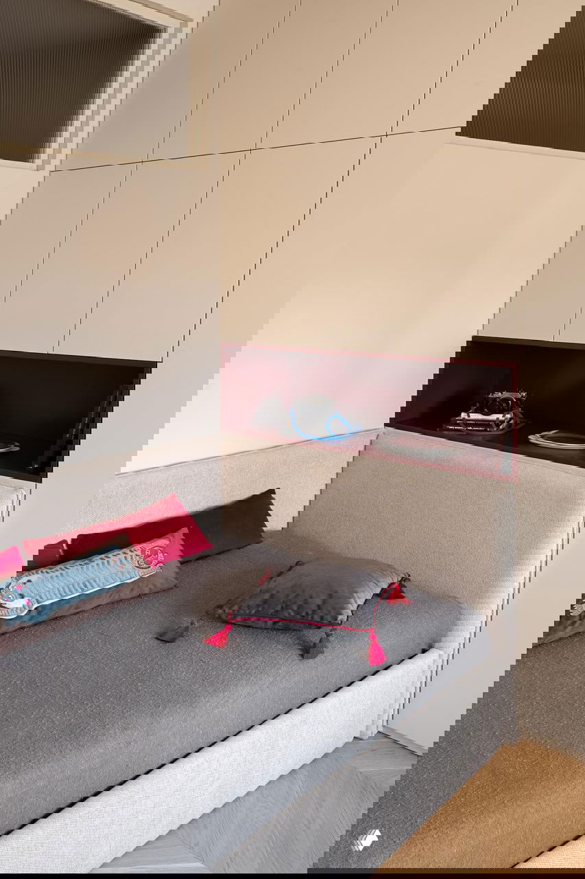 Спальная зона с низкой кроватью и встроенными шкафами: над изголовьем бордовая ниша, декоративные подушки и сдержанная цветовая гамма в текстиле.