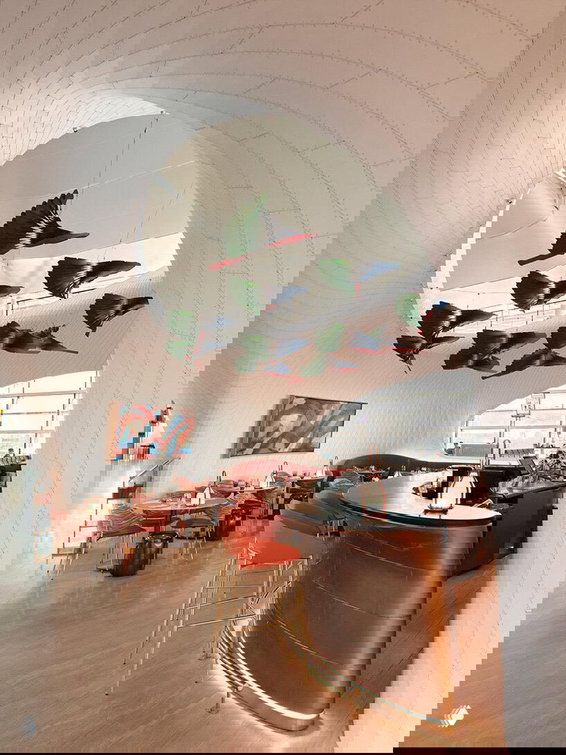 Внутреннее пространство: барная зона с волнообразной белой оболочкой, мягкими креслами и ярким подвесным декором в виде летящих птиц над столиками.