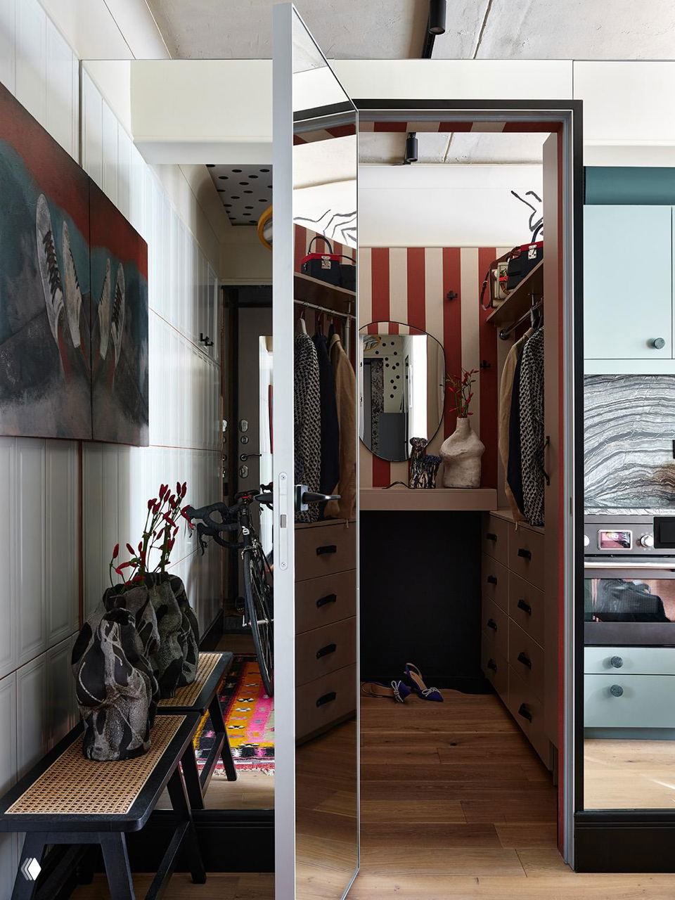 Уютная небольшая гардеробная за зеркальной дверью: узкая зона с аккуратными выдвижными ящиками, декор и яркая полосатая стена внутри.