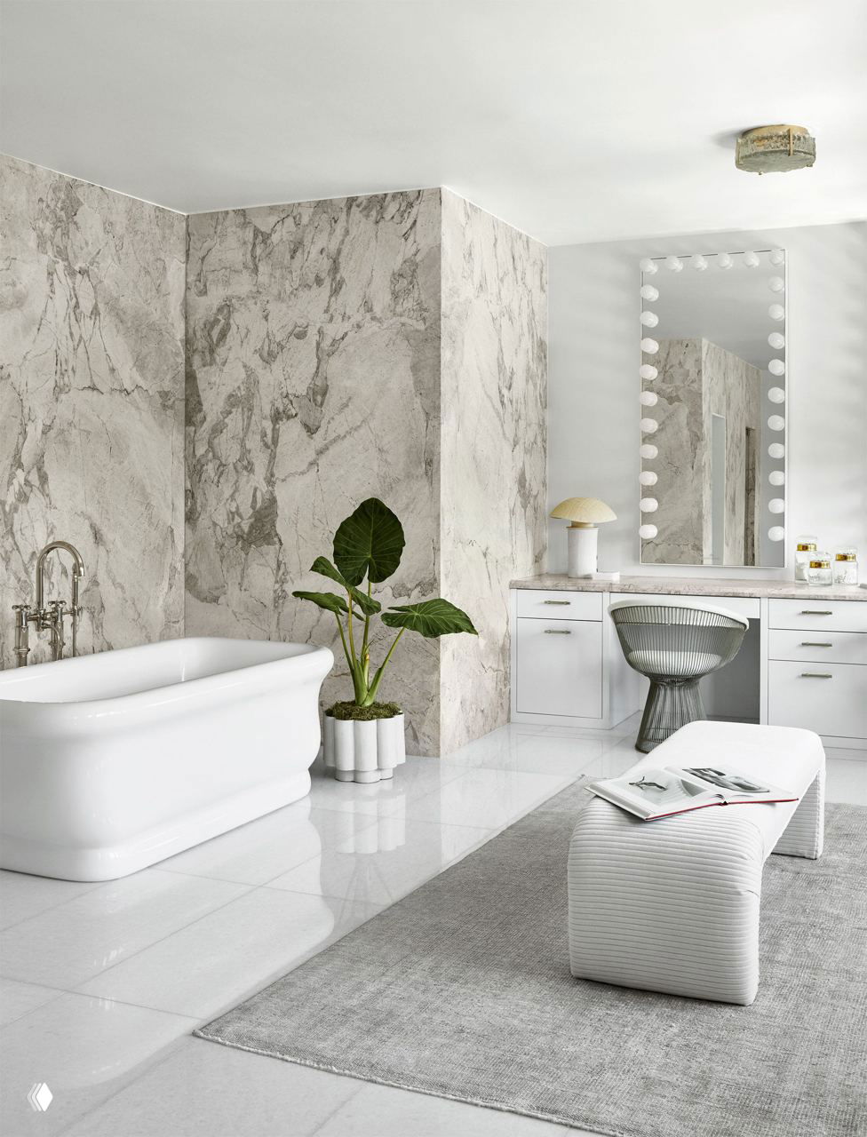 Светлая мраморная ванная комната с отдельной ванной, зеркалом в гримерном стиле и декоративным растением у ванны на фоне светлого пола.