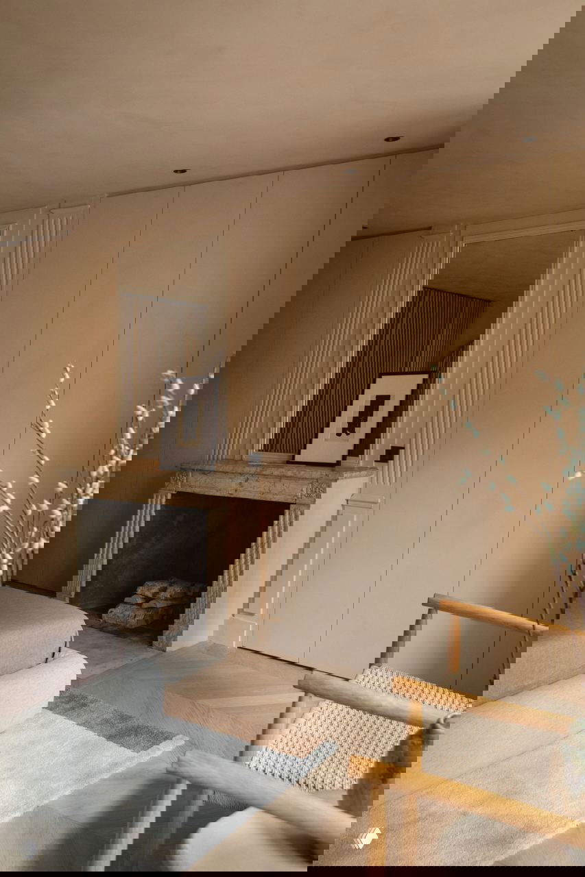 Угол спальни с камином и минималистичными панелями шкафа, мягкими бежевыми фактурами и деревянным стулом в японском духе.