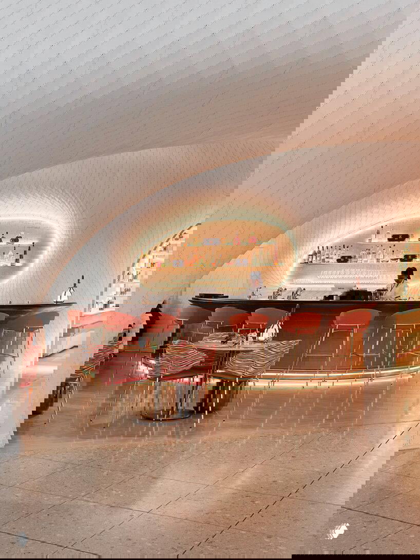 Крупный план барной стойки: металлическая стойка и стулья на фоне белых изогнутых панелей, подсветка подчёркивает плавные кривые пространства.