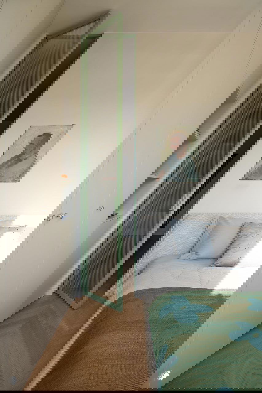 Маленькая спальня с зелёной рифлёной дверью, паркетом ёлочкой, картиной над изголовьем и контрастным текстилем на кровати — светлая, но насыщенная деталью.