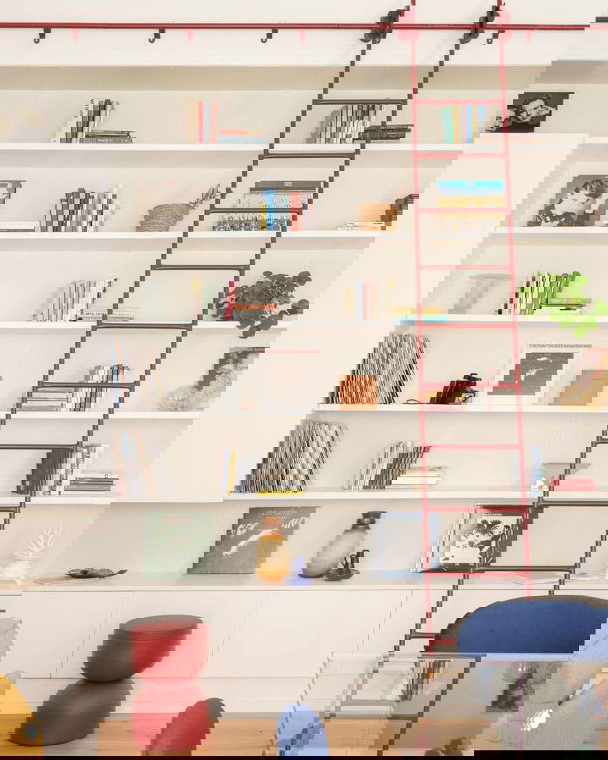 Стеллаж со сведениями о поп-арте и виниловыми пластинками, красная стремянка-лестница и декоративные предметы в светлом пространстве гостиной.