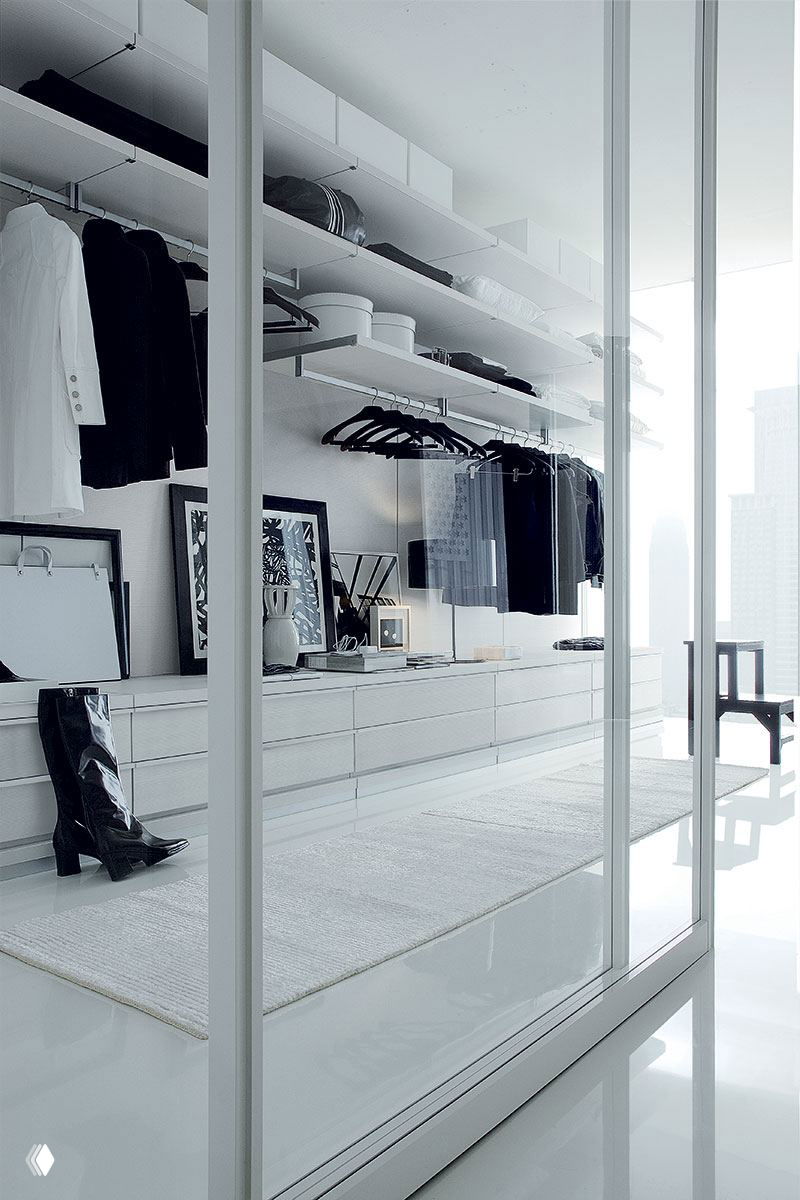 Стеклянные раздвижные двери открывают просторную монохромную гардеробную с длинными полками, вешалками и аккуратно расставленной обувью и аксессуарами.