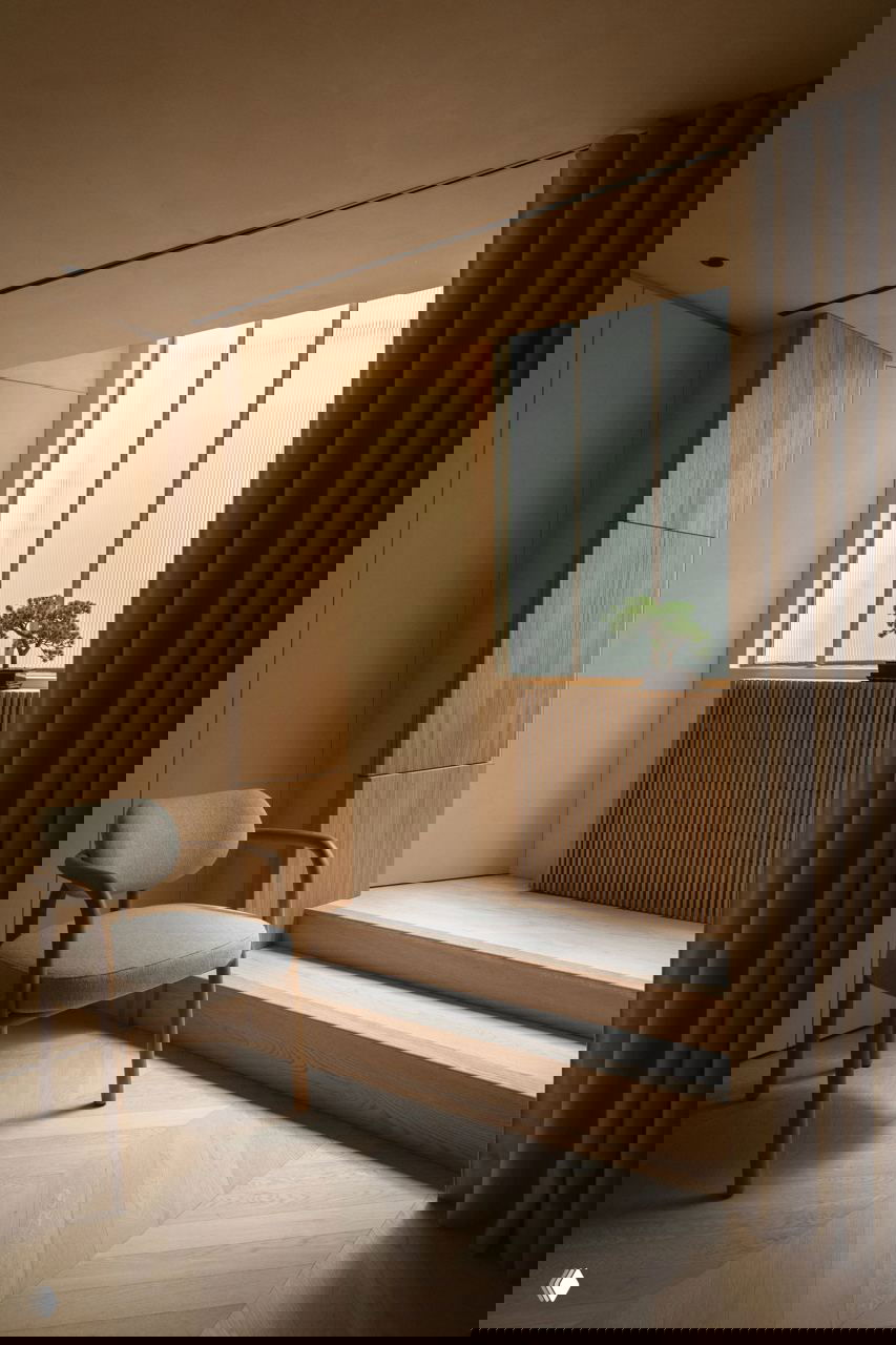 Низкий подъём с несколькими ступенями к окну, деревянный радиатор с вертикальными планками и маленькое бонсай-дерево на подоконнике.