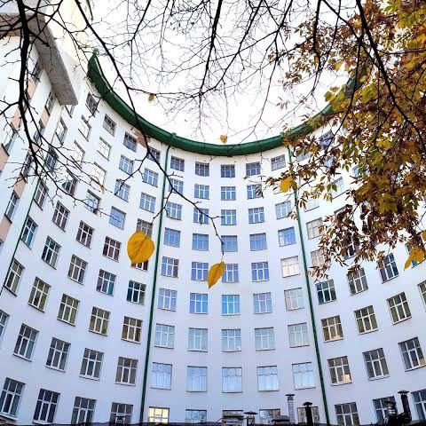 Внутренний двор округлого конструктивистского дома в Екатеринбурге: полукруглая фасадная стена, окна и осенние листья на переднем плане.