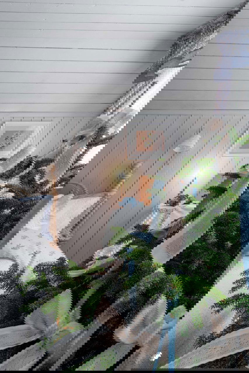 Вид на ёлку у кровати с большими текстильными бантами и светлой отделкой стен — спокойный деревенский стиль с уютными акцентами.