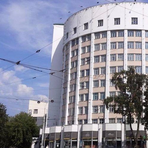 Фасад крупной круглой многоэтажки в конструктивистском стиле на фоне неба, где простая геометрия и много одинаковых окон формируют силуэт здания.